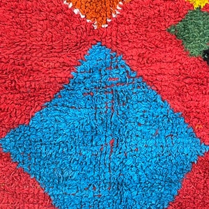 May include: A close-up of a colorful rug with a diamond pattern. The rug is made of a soft, fuzzy material and features shades of red, blue, orange, yellow, and green.
