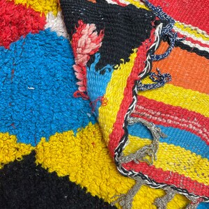 May include: A colorful woven rug with stripes of red, yellow, blue, and black. The rug has a fringe border and is made of a thick, textured material.