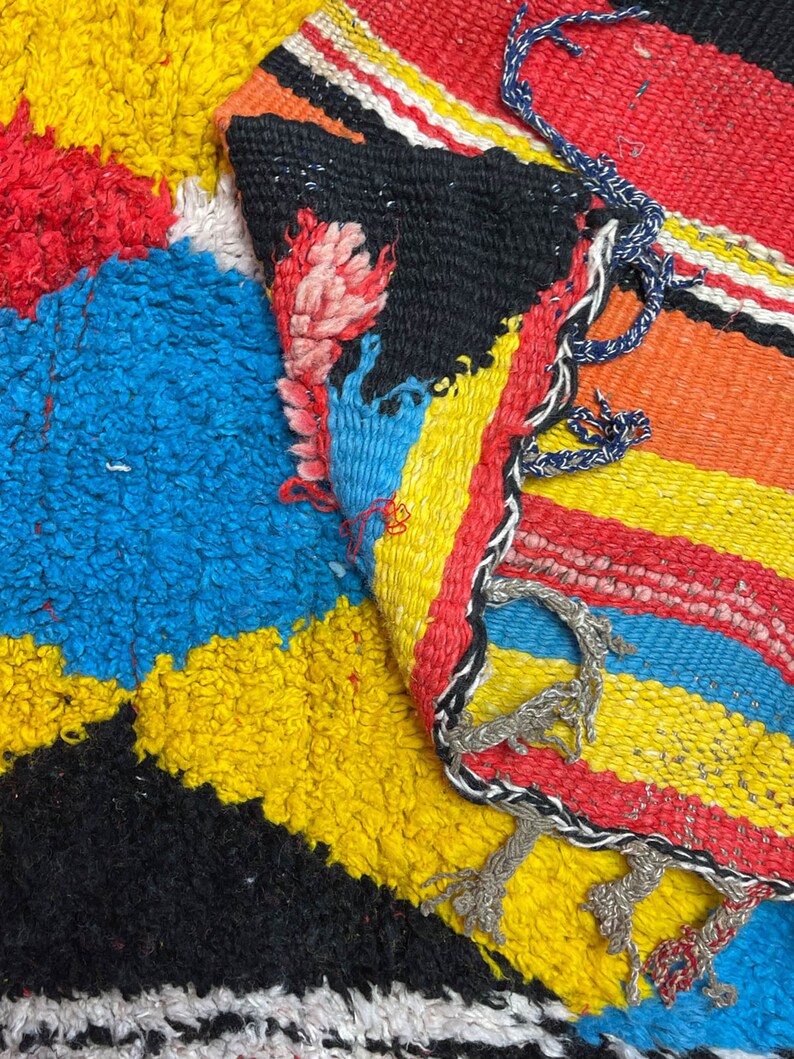 May include: A colorful woven rug with stripes of red, yellow, blue, and black. The rug has a fringe border and is made of a thick, textured material.
