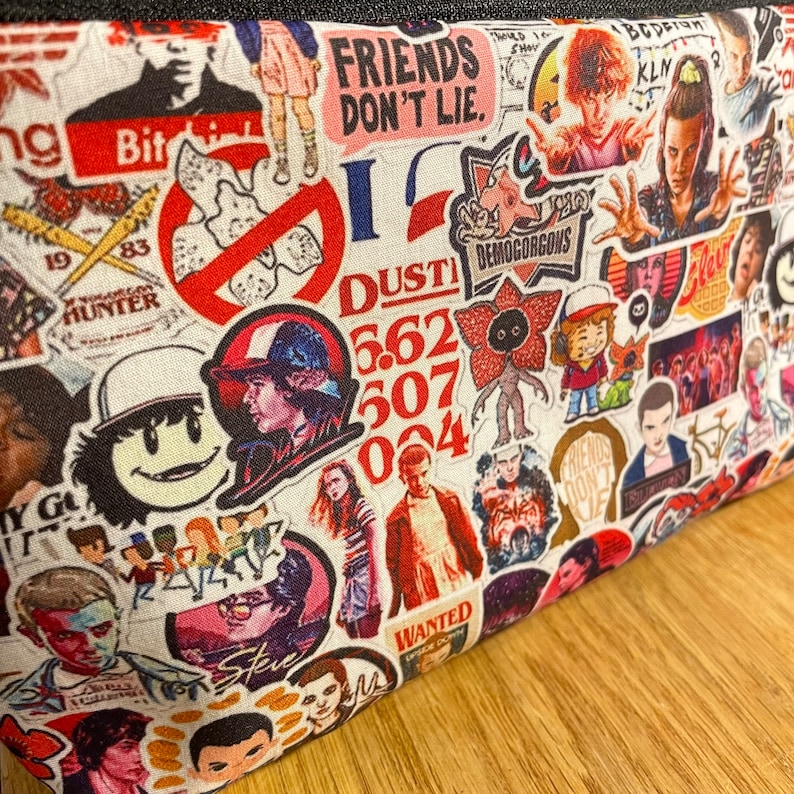 Puede incluir: Una bolsa de tela blanca cubierta de coloridas pegatinas con personajes y frases de la serie de televisi&oacute;n "Stranger Things". Las pegatinas incluyen im&aacute;genes de personajes, el Demogorgon y el texto "FRIENDS DON'T LIE."