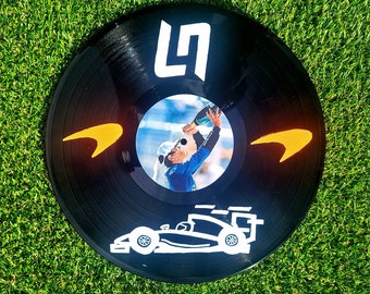 May include: Black vinyl record with a white "LN" logo, a photo of a person celebrating with a champagne bottle, and a white silhouette of a race car.