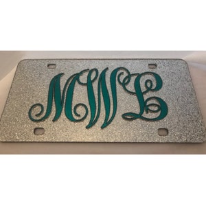 May include: Silver glitter license plate with teal monogram letters. The plate has four mounting holes and a rectangular shape. The monogram features the letters M, N, and L in a decorative script font.