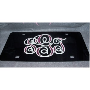 May include: Black license plate with a white and pink monogram of the letters "S.A.J."