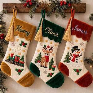Puede incluir: Tres calcetines navideños personalizados con puños de terciopelo en oro, verde y óxido. Los calcetines están bordados con los nombres Henry, Oliver y James, y decorados con motivos festivos que incluyen un tren, un reno y un muñeco de nieve.