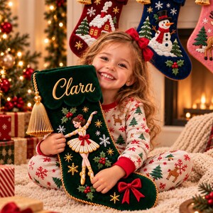 Könnte beinhalten: Ein dunkelgrüner Weihnachtsstrumpf aus Samt mit einer gestickten Ballerina, einer goldenen Quaste und dem Namen Clara. Der Strumpf ist mit Schneeflocken, Stechpalmen und einer roten Schleife verziert. Drei weitere Strümpfe mit den Namen Amelia, James und Sophie hängen darüber.