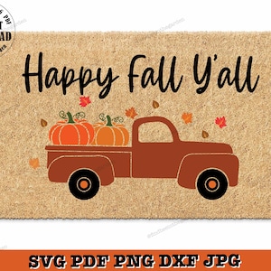 May include: A brown doormat with the text "Happy Fall Y'all" in black lettering. A cartoon image of a red pickup truck with a bed full of orange pumpkins is below the text.  The truck is driving on a brown road with orange and red leaves scattered around it.