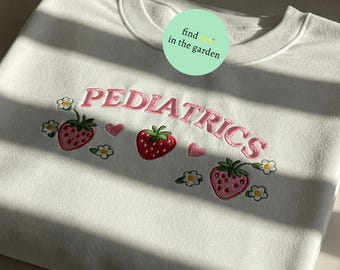 May include: White sweatshirt with pink embroidered text "PEDIATRICS" and strawberry designs.