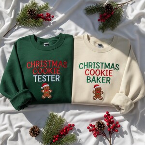 以下が含まれることがあります： 2つのクリスマスをテーマにしたスウェットシャツ。1つは濃い緑色で、「CHRISTMAS COOKIE TESTER」が赤と白で刺繍され、ジンジャーブレッドマンがいます。もう1つはクリーム色で、「CHRISTMAS COOKIE BAKER」が緑と赤で刺繍され、ジンジャーブレッドマンがいます。
