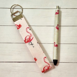 May include: A pink and white keychain with a flamingo design and a matching pink and white pen with a flamingo design.