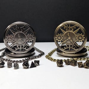 May include: Two round pocket watch cases with intricate gear and sunburst cutouts, one in silver and one in antique brass. Each case is attached to a matching metal chain and is accompanied by a set of seven small polyhedral gaming dice.