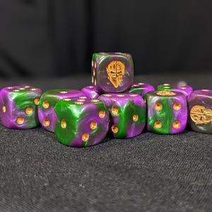 May include: A collection of ten dice in shades of purple and green with gold-colored pips. Some dice feature a gold skull emblem. The dice are arranged on a dark, textured surface, creating a visually striking display.