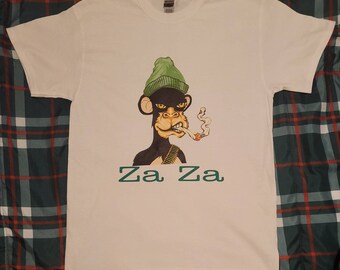 May include: White t-shirt with a cartoon image of a monkey wearing a green hat and smoking a cigarette. The text "Za Za" is printed below the monkey.