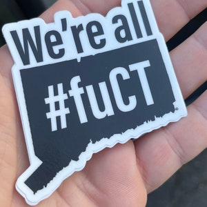 May include: A white sticker with a black outline in the shape of the state of Connecticut. The sticker says "We're all #fuCT" in white letters.