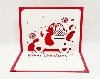 May include: A red and white pop-up card with a white silhouette of a scooter carrying gifts and candy canes. The card reads "Merry Christmas".