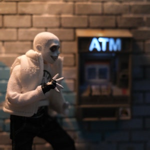 Puede incluir: Una figura blanca con un guante negro y una chaqueta blanca se encuentra frente a un cajero autom&aacute;tico con la palabra "ATM" en letras blancas sobre un fondo marr&oacute;n.