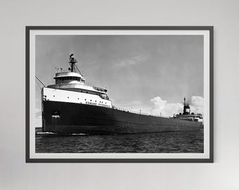May include: Black and white framed photograph of the Edmund Fitzgerald, a large freighter ship, sailing on water under a cloudy sky. The ship's name is visible on the side. The image is in a black frame.