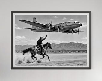 May include: A black and white framed print featuring a cowboy on horseback waving at a low-flying American Airlines propeller airplane. The scene is set in a desert landscape with mountains in the background and dust kicking up from the ground.