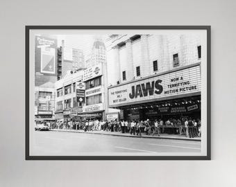 May include: A black and white framed photograph of a city street scene featuring a movie theater marquee displaying the text JAWS, NOW A TERRIFYING MOTION PICTURE, THE TERRIFYING NO. 1 BEST SELLER, along with the names Roy Scheider, Robert Shaw, and Richard Dreyfuss.