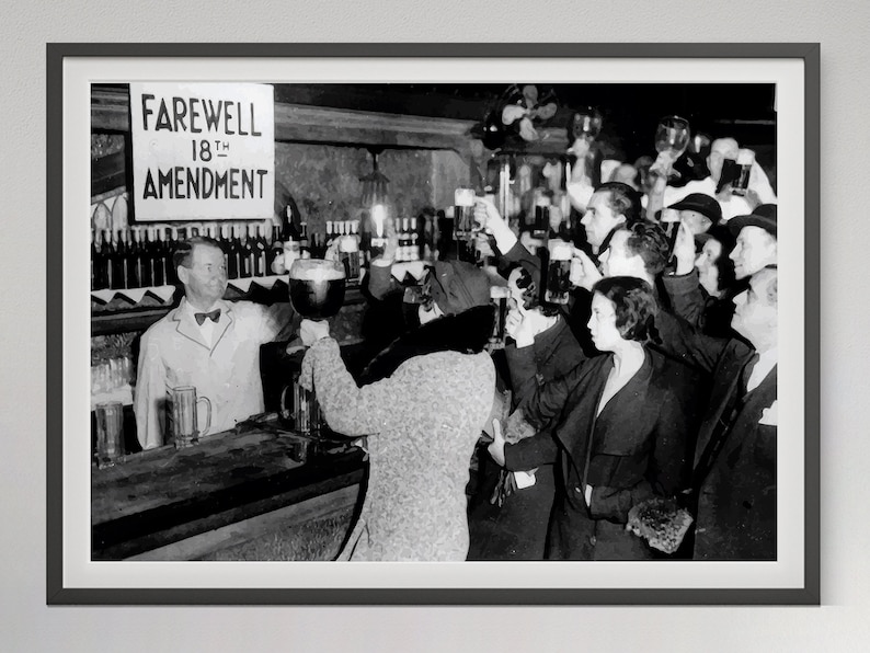 May include: A black and white photograph of a group of people celebrating the repeal of the 18th Amendment, which prohibited the sale of alcohol in the United States. A sign reads "Farewell 18th Amendment".