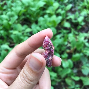 May include: A close-up of a pink and red ruby crystal. The crystal is rough and has a natural, unpolished look.