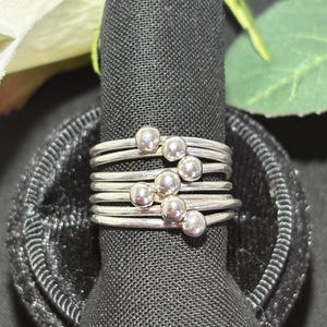 May include: A multi-band ring crafted from polished silver-toned metal, featuring five individual thin bands stacked together. Each band is accented with a small, smooth, spherical bead, with the beads arranged in a diagonal pattern across the front.