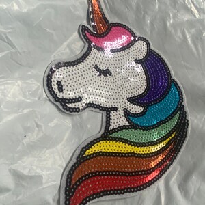 May include: A white unicorn with a rainbow mane and tail made of sequins. The unicorn has a pink horn and a pink ear.
