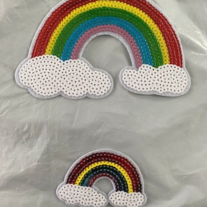 May include: Two rainbow-coloured sequin patches with white cloud shapes. The larger patch has a red, yellow, green, blue, and pink rainbow. The smaller patch has a red, yellow, green, and blue rainbow.