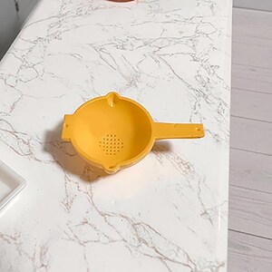 Może przedstawiać: Ż&oacute;łte plastikowe sitko z uchwytem. Sitko ma okrągłą miseczkę z małymi otworami i uchwytem rozciągającym się w prawo. Przeznaczone jest do przecedzania płyn&oacute;w lub drobnych produkt&oacute;w spożywczych.