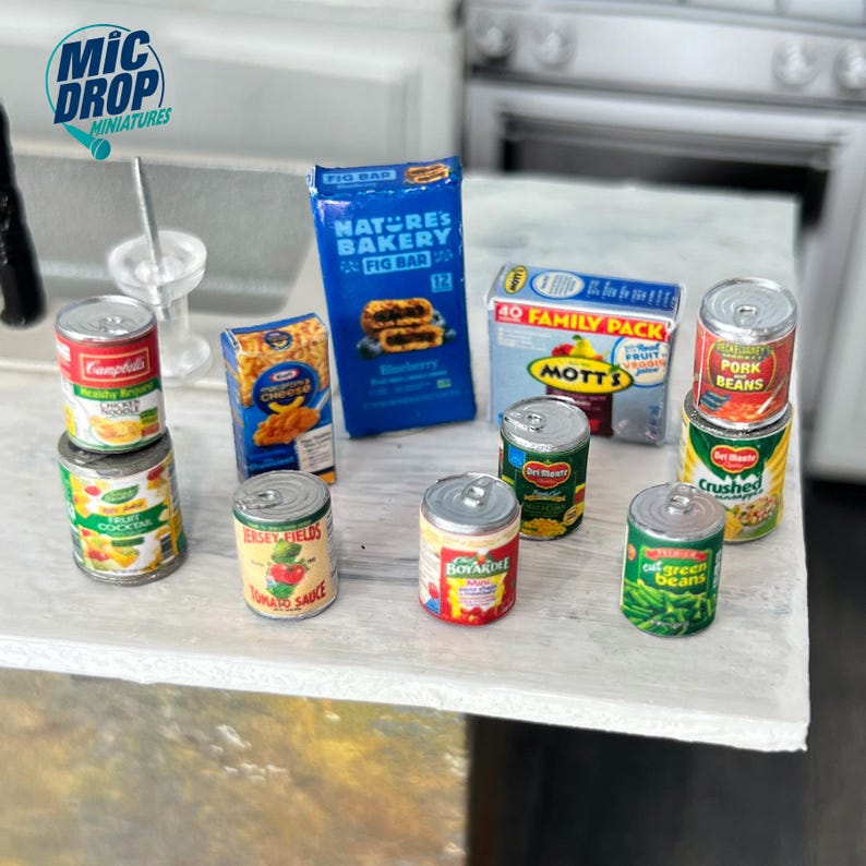 May include: A collection of miniature canned goods, including tomato sauce, fruit cocktail, green beans, pork and beans, and crushed tomatoes. There are also miniature boxes of fig bars, macaroni and cheese, and a family pack of Mott's applesauce.