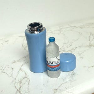May include: A light blue water bottle with a silver top, a small clear water bottle with a blue cap, and a blue cap. The small bottle has a label with the word "QUAELL" on it.