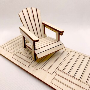 May include: A wooden model of a classic Adirondack chair, with a natural wood finish. The chair is assembled and sitting on a sheet of plywood with cut-out pieces for the chair's parts.