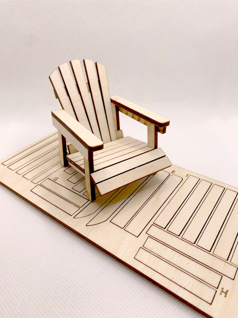 May include: A wooden model of a classic Adirondack chair, with a natural wood finish. The chair is assembled and sitting on a sheet of plywood with cut-out pieces for the chair's parts.