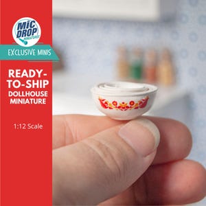 Może przedstawiać: Zestaw trzech gniazdujących się misek w kolorze białym z czerwono-żółtym wzorem kwiatowym. Miski są miniaturami do domków dla lalek w skali 1:12.