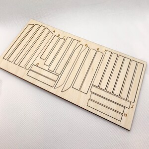 May include: A sheet of wood with various shapes and sizes cut out, labeled with letters A through J. The wood is light brown and the letters are gold.