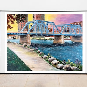 K&ouml;nnte beinhalten: Ein Gem&auml;lde einer blauen Br&uuml;cke &uuml;ber einem Fluss mit einer Stadtkulisse im Hintergrund. Der Fluss ist blau und der Himmel ist ein Farbverlauf von Rosa und Lila. Am Flussufer befinden sich Steine und gr&uuml;nes Gras.