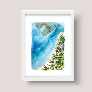 May include: A watercolor painting of a beach scene from an aerial view. The painting features a curved shoreline with turquoise water, a sandy beach, and a small island with green trees. The painting is framed in a white frame.