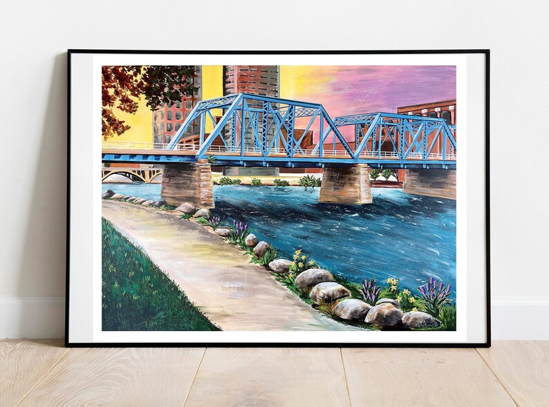 K&ouml;nnte beinhalten: Ein Gem&auml;lde einer blauen Br&uuml;cke &uuml;ber einem Fluss mit einer Stadtkulisse im Hintergrund. Der Fluss ist blau und der Himmel ist ein Farbverlauf von Rosa und Lila. Am Flussufer befinden sich Steine und gr&uuml;nes Gras.