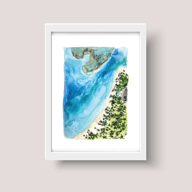 May include: A watercolor painting of a beach scene from an aerial view. The painting features a curved shoreline with turquoise water, a sandy beach, and a small island with green trees. The painting is framed in a white frame.