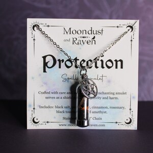 Puede incluir: Un collar de plata con un colgante de vial de vidrio lleno de hierbas y un amuleto de pentagrama. La tarjeta dice "Moondust and Raven Protection Spell Amulet". Hecho con cuidado e intenci&oacute;n, este amuleto encantador sirve como escudo contra la negatividad y el da&ntilde;o. Incluye: sal negra, turmalina negra, canela, romero y amatista.