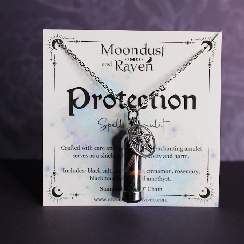 Puede incluir: Un collar de plata con un colgante de vial de vidrio lleno de hierbas y un amuleto de pentagrama. La tarjeta dice "Moondust and Raven Protection Spell Amulet". Hecho con cuidado e intenci&oacute;n, este amuleto encantador sirve como escudo contra la negatividad y el da&ntilde;o. Incluye: sal negra, turmalina negra, canela, romero y amatista.