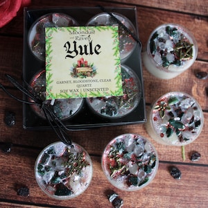 Puede incluir: Una colección de velas de cera de soja con temática de Yule, algunas con cristales decorativos y purpurina. Las velas están en recipientes transparentes, con un juego de cuatro velas y dos velas individuales. La etiqueta dice "Moondust and Raven Yule".