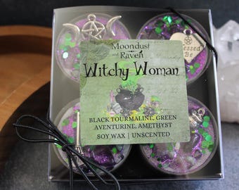 May include: Set of four tealight candles in a clear box. Each candle has a different crystal and green glitter embedded in the wax. The box has a label that reads "Moondust and Raven Witchy Woman" and lists the crystals used: Black Tourmaline, Green Aventurine, Amethyst. The label also states "Soy Wax | Unscented".