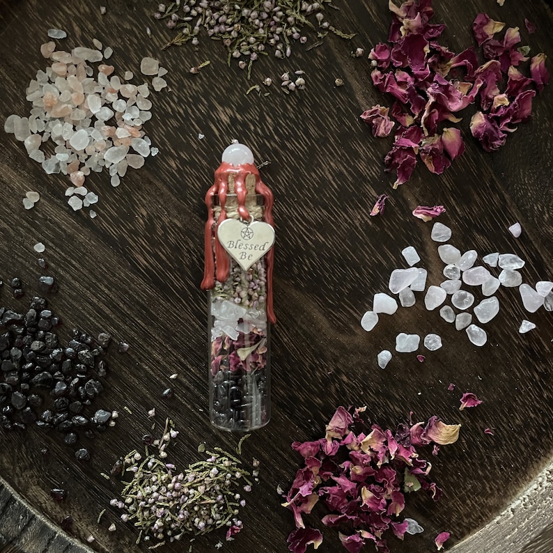 May include: A glass bottle filled with dried herbs, rose petals, and crystals. The bottle is sealed with a red wax seal and has a silver charm that says "Blessed Be".
