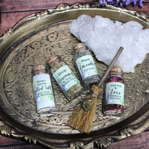 May include: Four small glass jars with cork stoppers containing salt, dried rosemary, dried lavender, and dried flower petals. Each jar has a label with text and a small broom with a crescent moon charm. A large white quartz crystal is included.