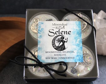 May include: A set of four unscented soy wax tea lights in a clear box. Each tea light features a silver charm with a moon and stars design. The box has a label that reads "Moondust and Raven Selene Moonstone, Selenite, Sodalite Soy Wax | Unscented".