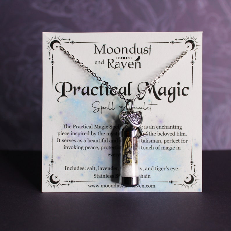 Puede incluir: Un collar de plata con un peque&ntilde;o dije de vidrio lleno de hierbas y cristales. El dije est&aacute; etiquetado como "Practical Magic Spell Amulet" y la tarjeta dice "Moondust and Raven".