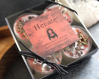 Könnte beinhalten: Set aus vier roten Teelichtern aus Sojawachs mit eingebetteten Kristallen und Charms. Das Etikett lautet "Moonlight and Raven Hecate, Labradorite, Garnet, Black Tourmaline, Soy Wax | Unscented".