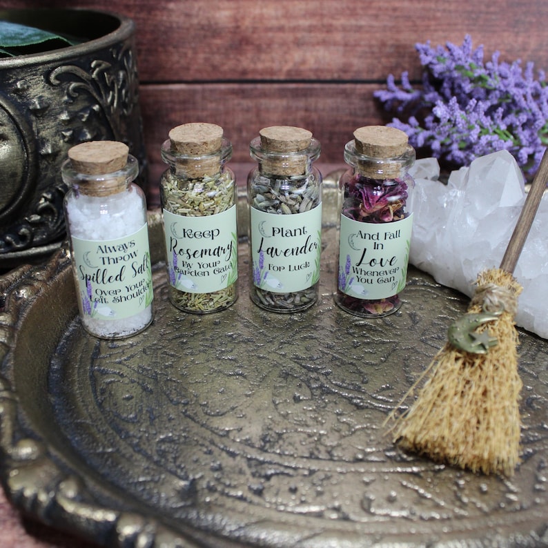May include: Four small glass jars with cork stoppers containing white salt, dried rosemary, dried lavender, and dried flower petals. Each jar features a label with text including Always Throw Spilled Salt, Keep Rosemary By Your Garden Gate, Plant Lavender For Luck, and And Fall In Love Whenever You Can.