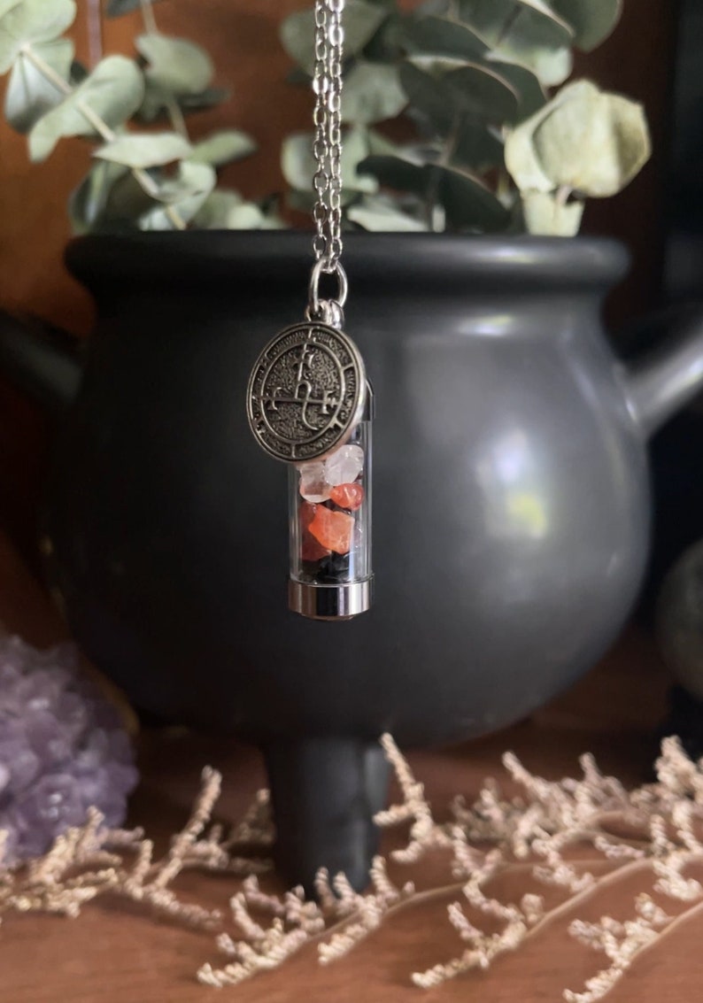 Handmade potion bottle necklace filled with assorted crystals including amethyst, carnelian, and quartz. The bottle is attached to a silver chain with an intricate charm. Perfect for those who appreciate unique jewelry with a touch of magic.