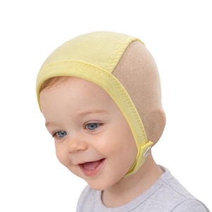 May include: A light yellow baby bonnet with a mesh back and a yellow trim. The bonnet has a strap that fastens with a small white button. The baby is wearing a gray shirt and has blue eyes.